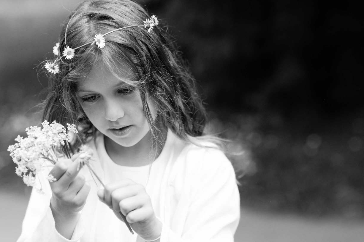 A young girl in a daisy chain circlet threads more daisies during her portrait session in the wilds of Kew Gardens, on the edge of London.