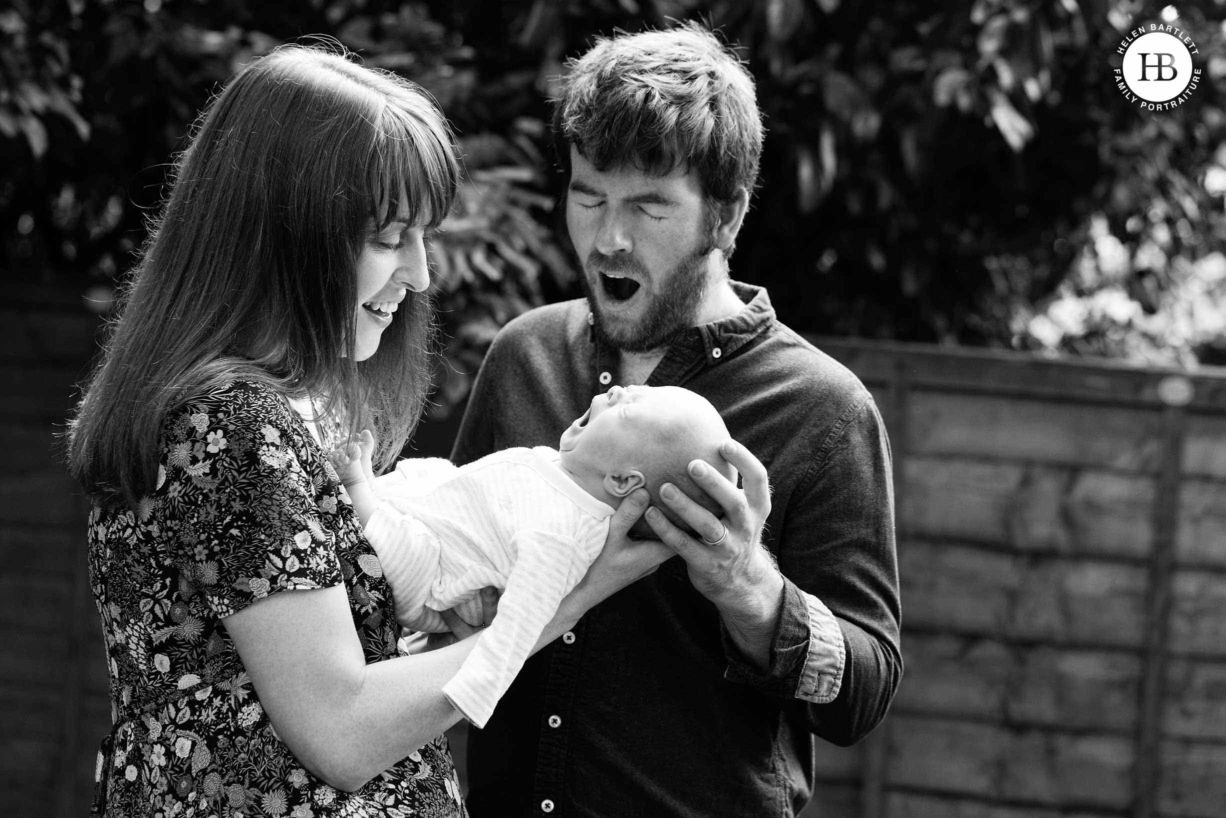 Two parents with their newborn have photos taken in their garden. Read the complete guide to having newborn photos taken at home.