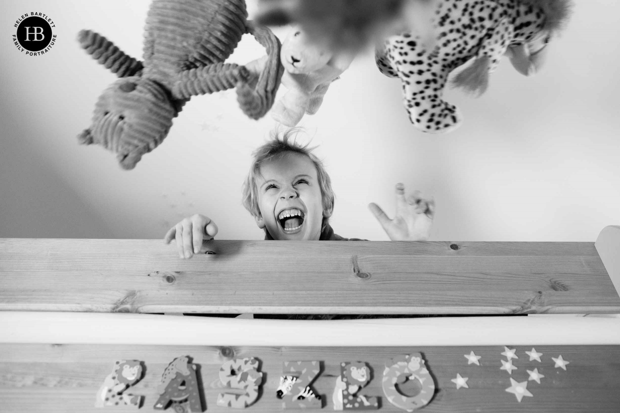 A boy plays in his bedroom, throwing his toys in the air during his family photo shoot