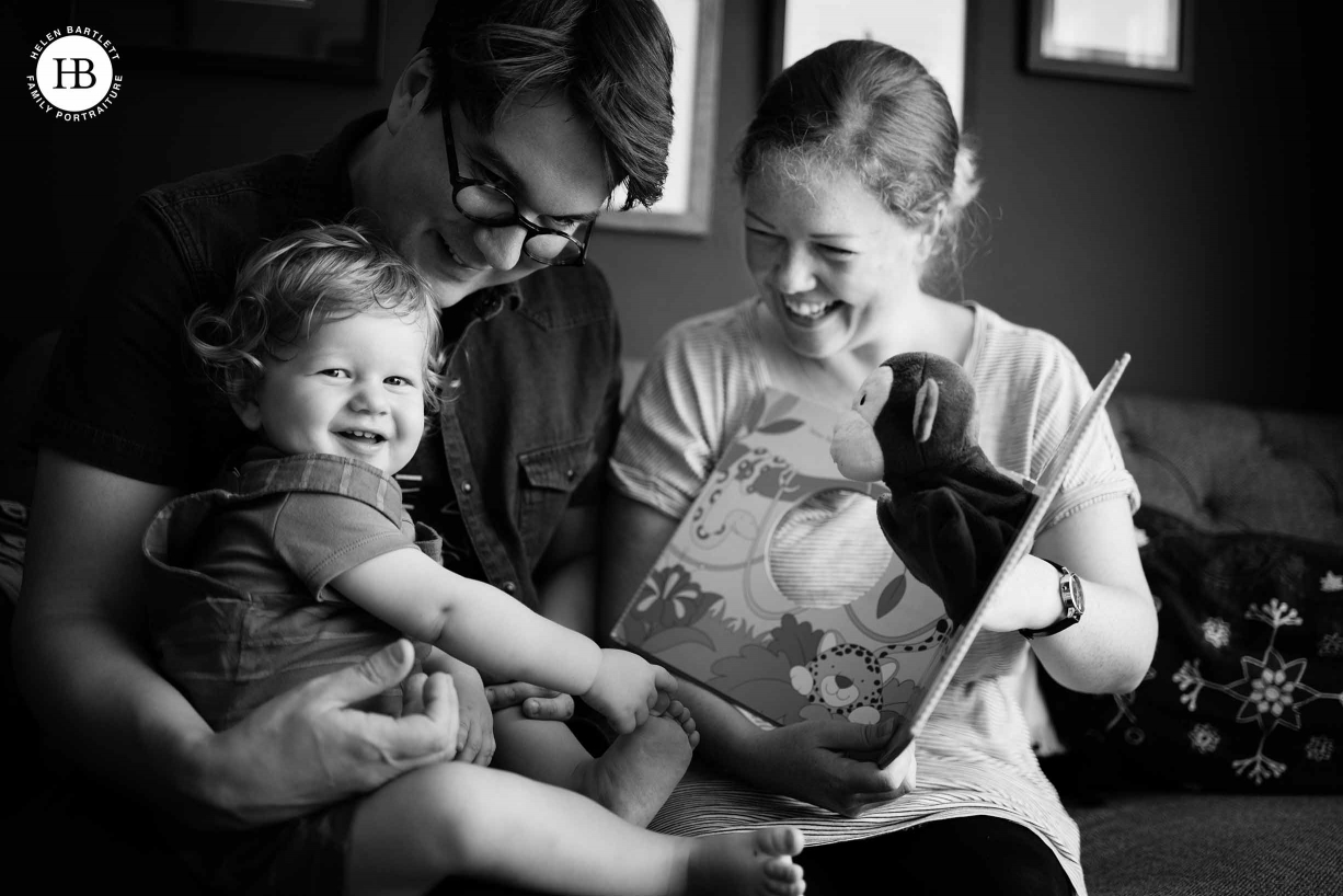 Family reading a book and laughing at a monkey hand puppet on the sofa