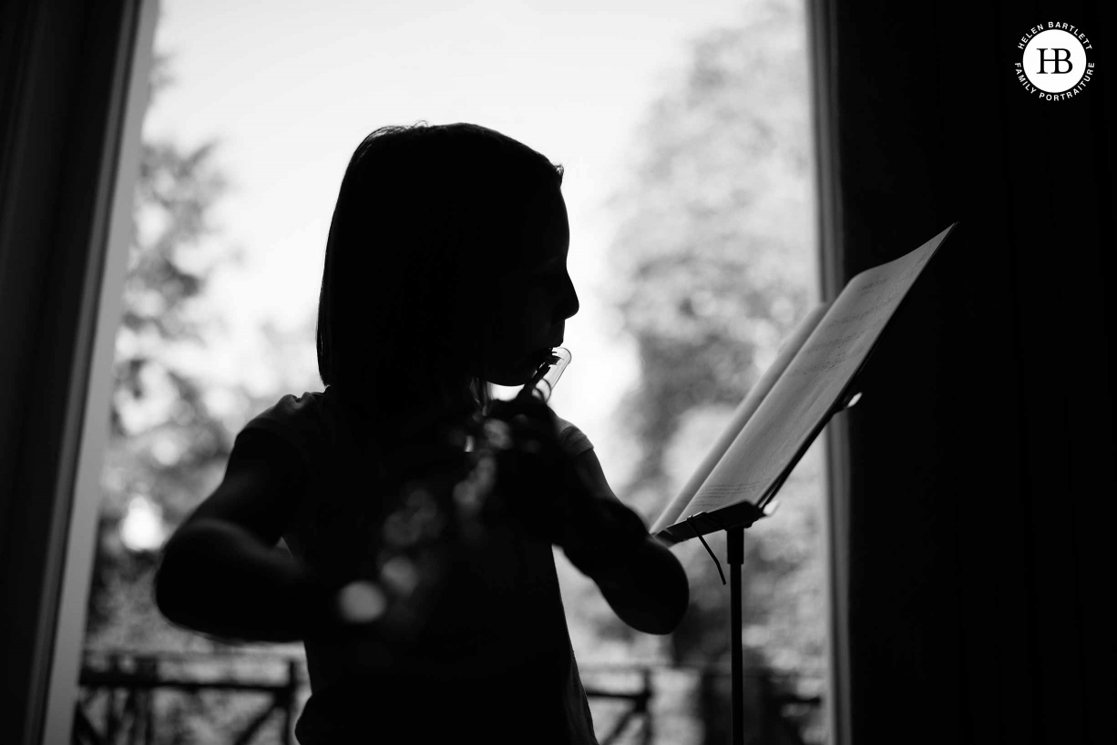 A home photo shoot: a girl practises her flute and is photographed in silhouette.