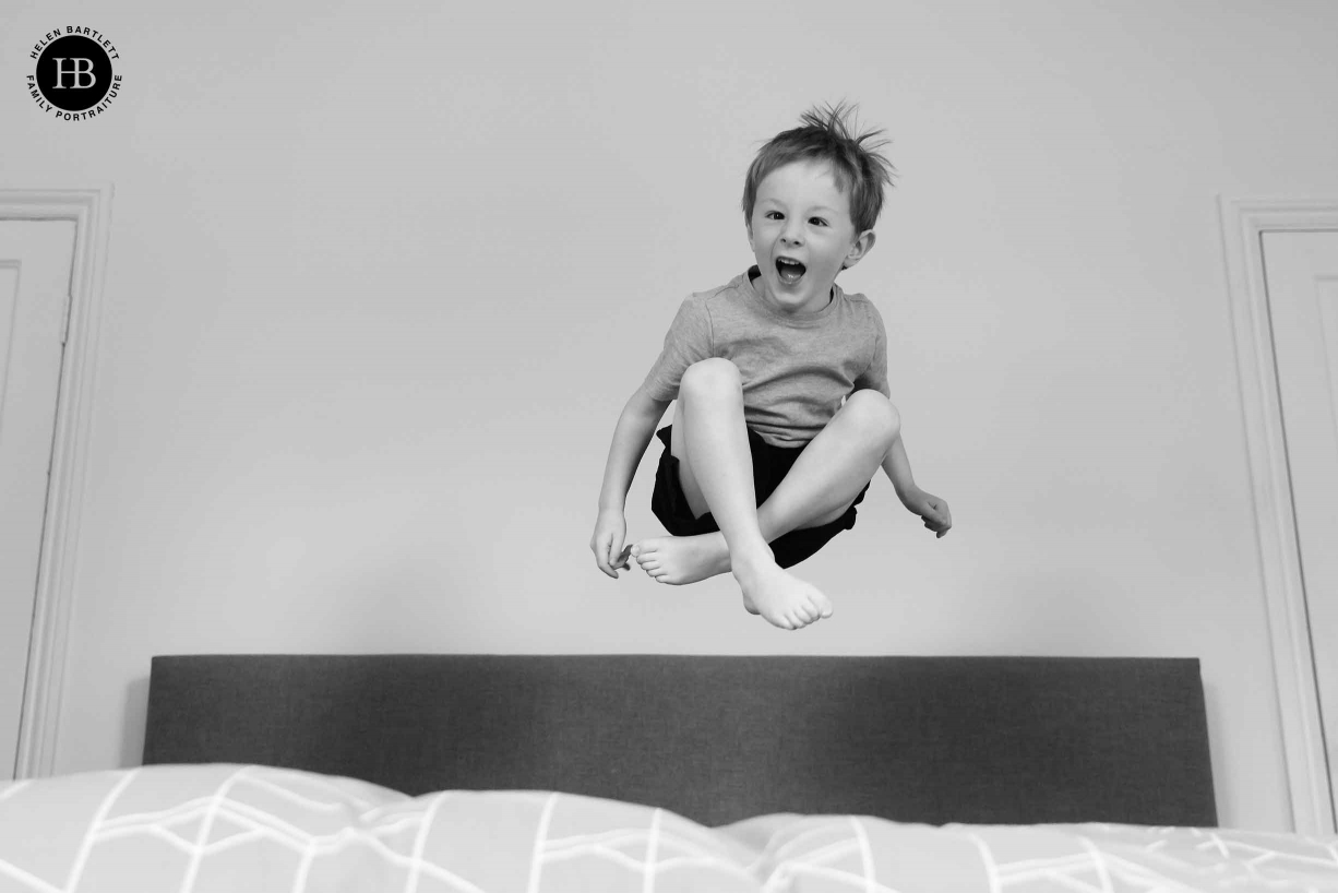 Little boy jumps on a bed, he is caught mid-air with his legs crossed. Showing the face-tracking autofocus of Canon EOS R5