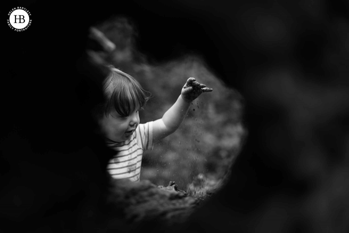 Little boy plays with mud and drops grains of mud and sand from his hand. Shot through a hole in a fallen tree for an interesting composition showing the benefits of the vari-angle screen on the EOS R5