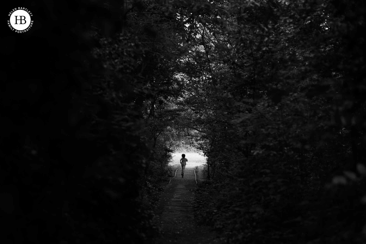 Boy running through a tunnel of undergrowth to the light field beyond, black and white