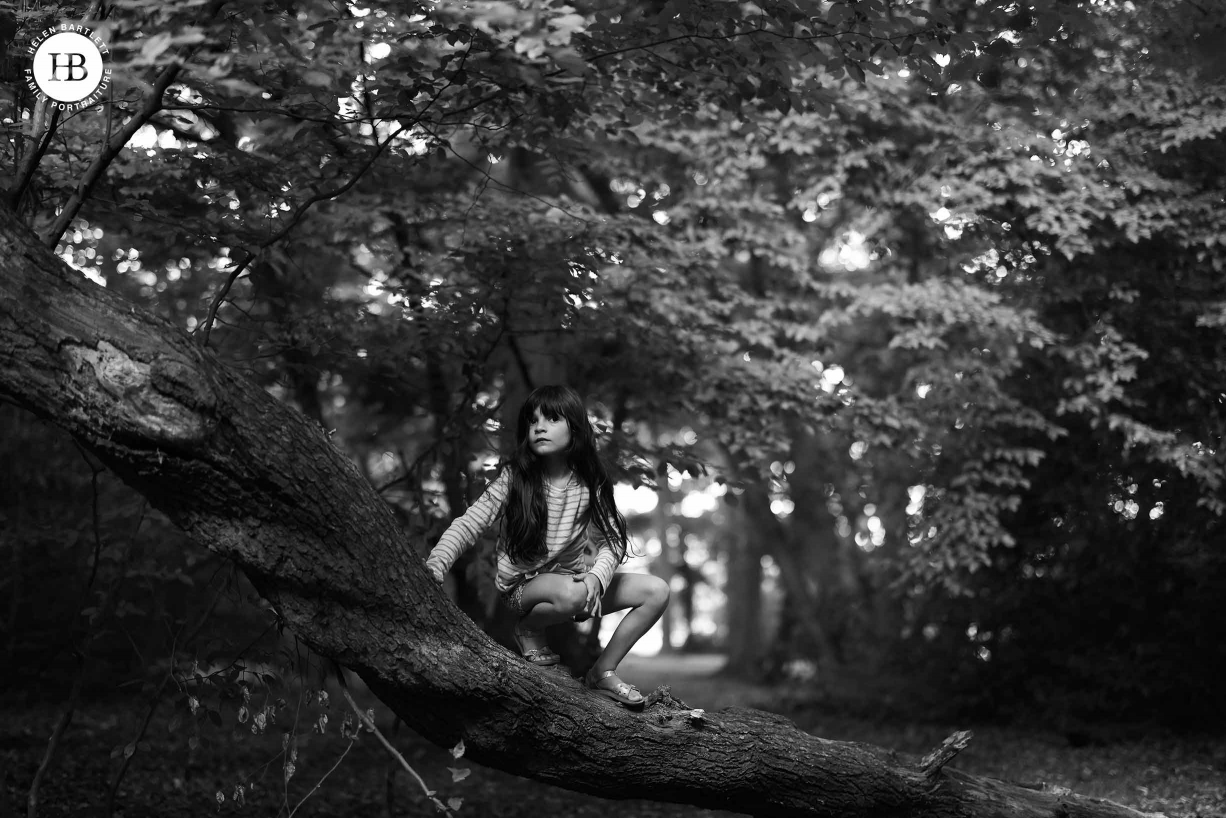 Little girl crouches on a tree trunk in a forest. Image shows incredible tones and dynamic range of 45mp EOS R5 files