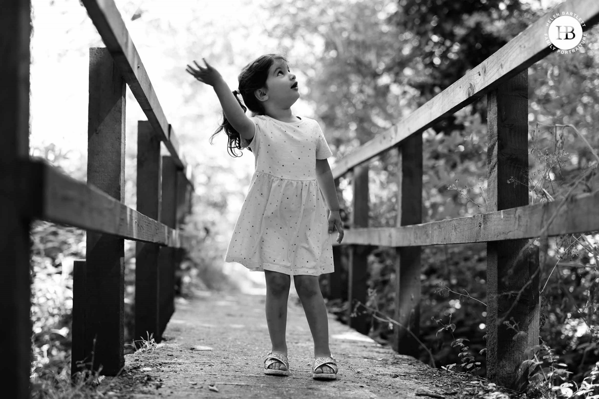 Little girl stands on a wooden bridge looking up and waving.