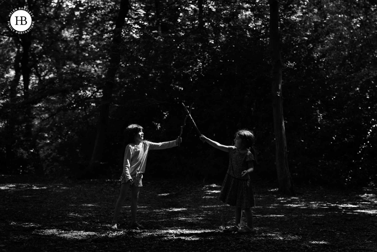 Two girls sword fight in a patch of sunlight in the woods. High contrast, dark image to show how the EOS R5 focuses well in difficult lighting conditions.