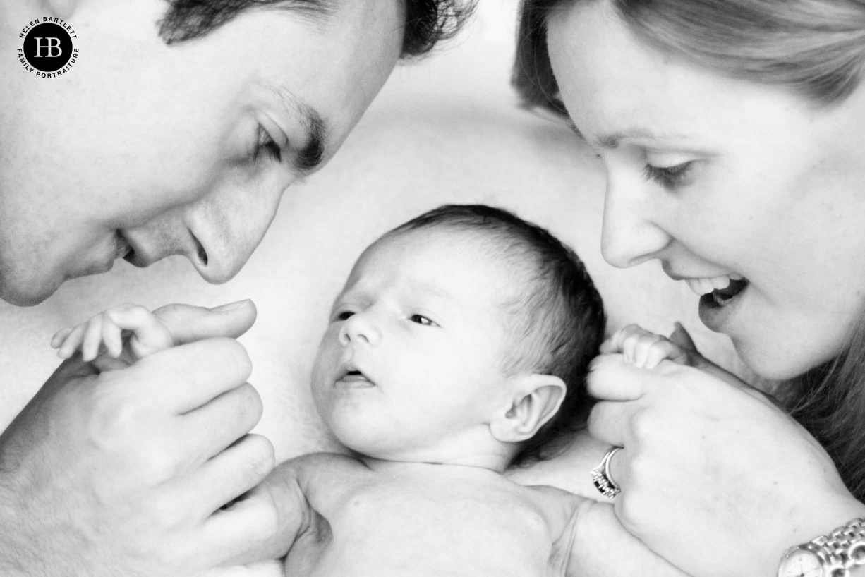 mum dad and newborn baby snuggle on a duvet in the shade during a socially distanced outdoor newborn photography session in their garden