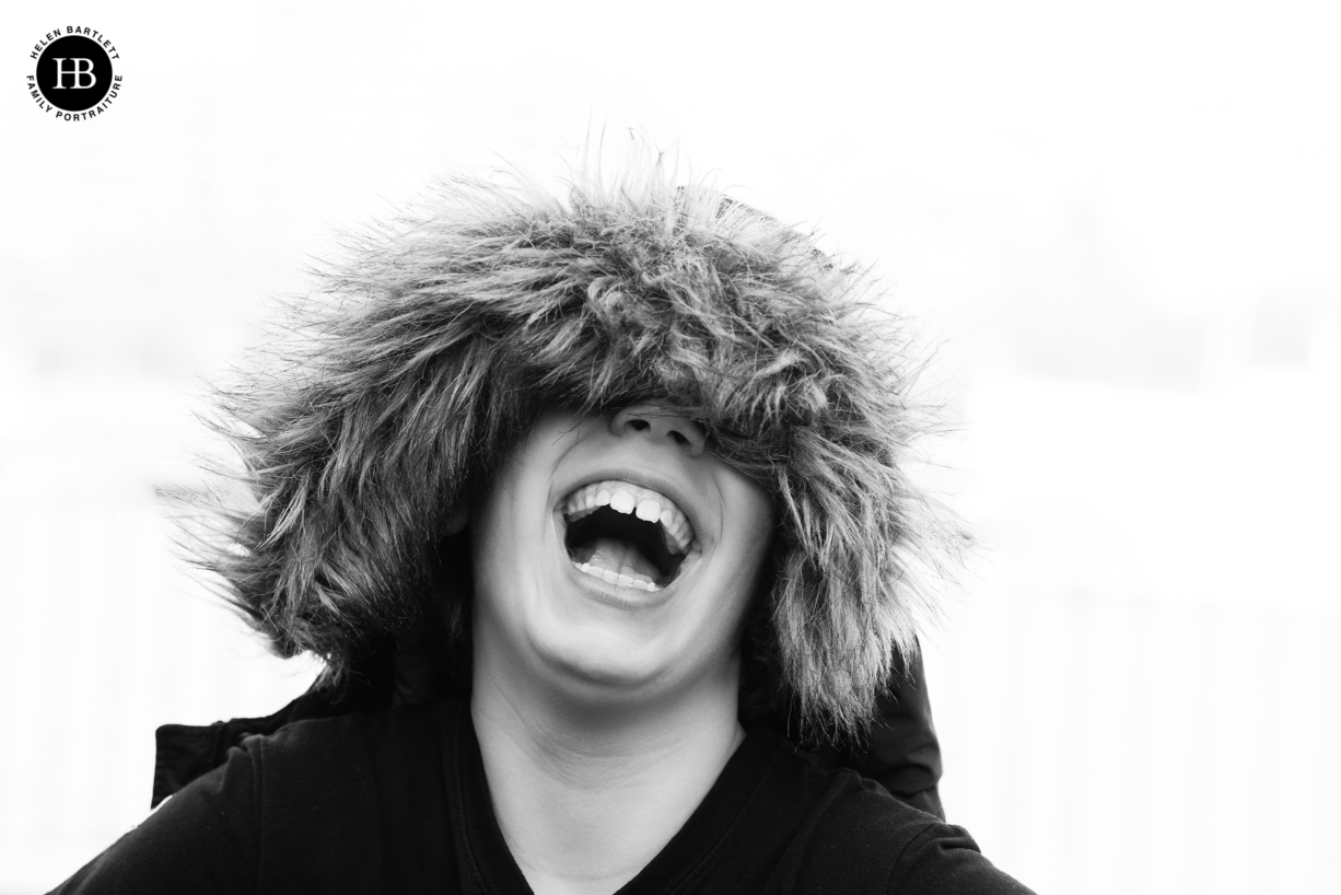 boy laughs under the hood of a parker jacket to show the benefit of warm clothing on a family photo shoot