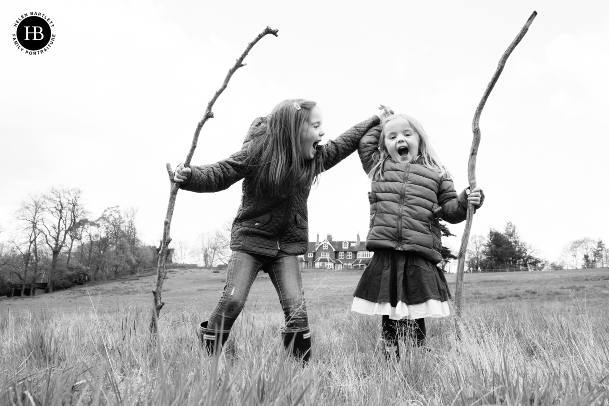 two little girls laugh holding sticks, one wearing a skirt the other wearing trousers. Dress for your personality when choosing your outfit for family photo shoot