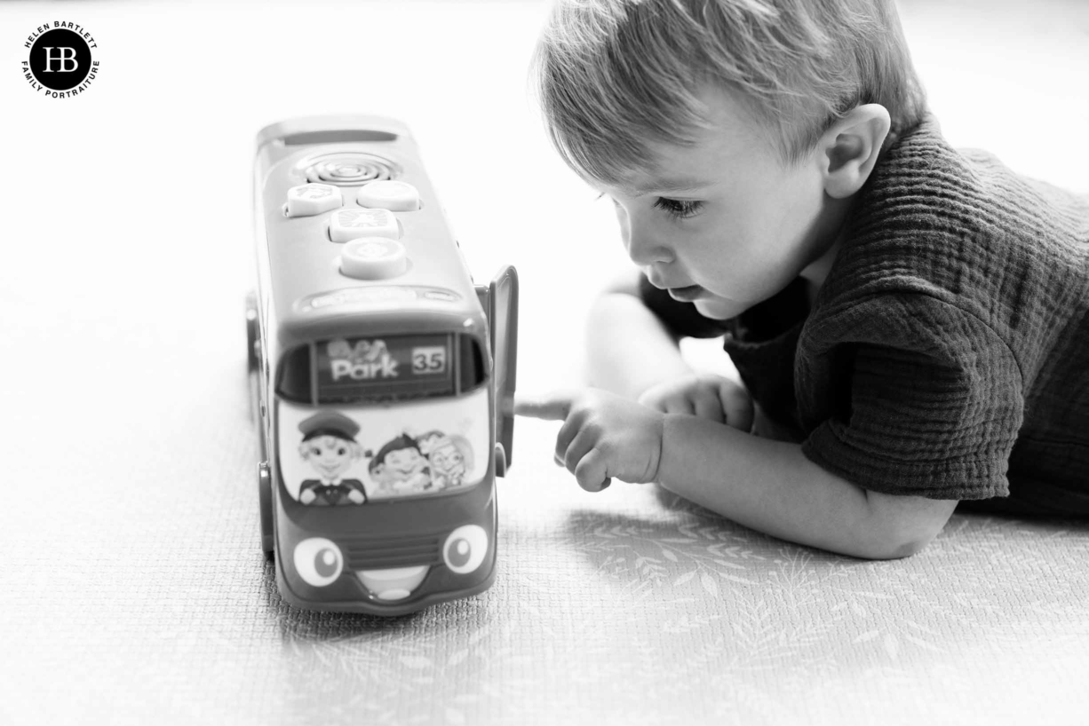 black and white professional photo of little boy playing with toy bus