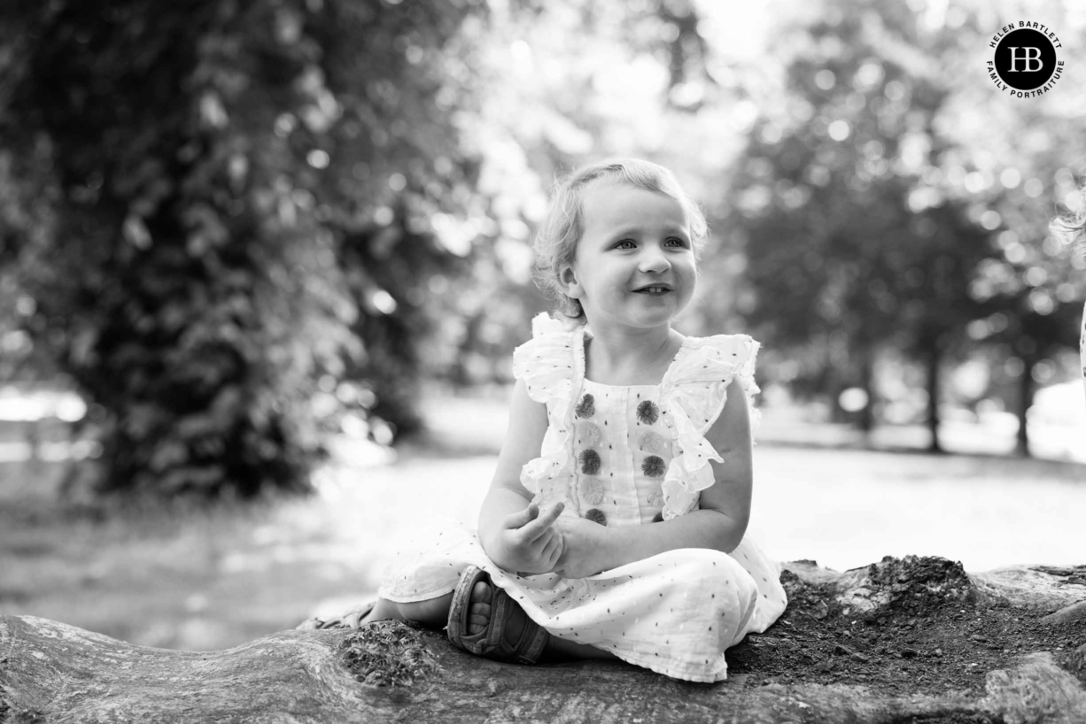 little girl sits on a fallen tree in Victoria park during an east London family photography session