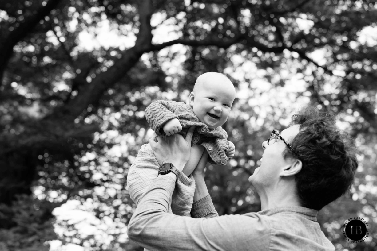 dad holds baby in the air and they both laugh in beautiful black and white family photo