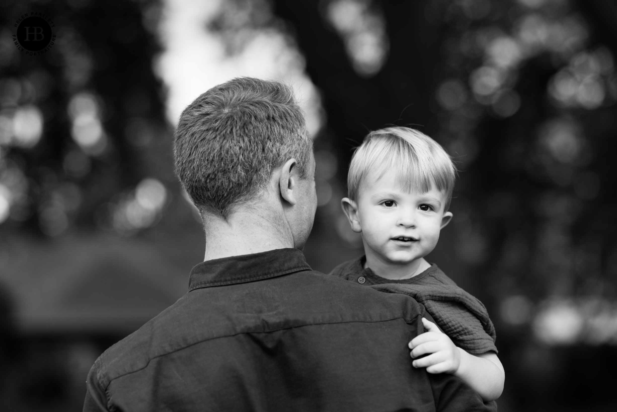 son looks back over fathers shoulder on clapham common during professional family photo shoot