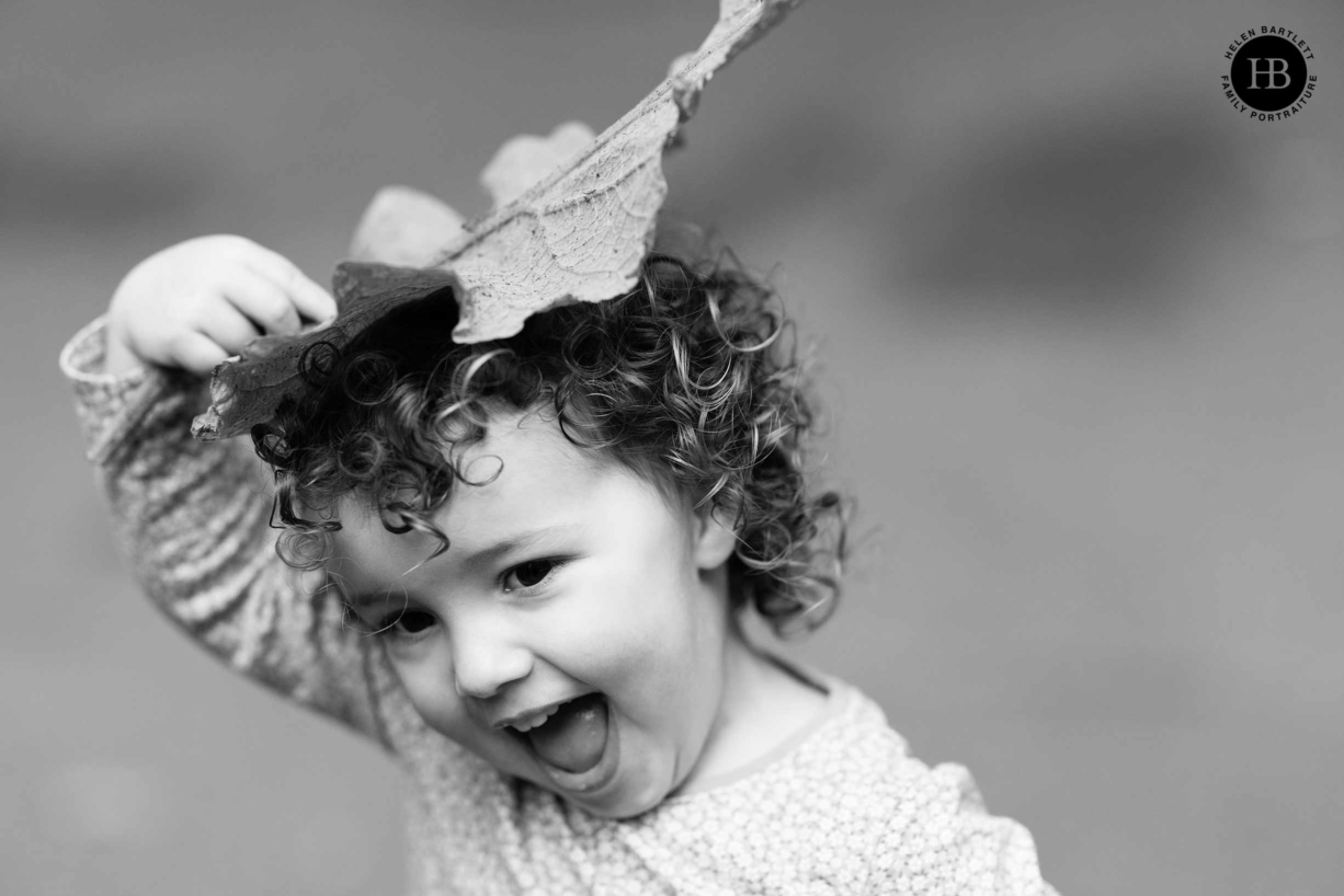 little girl laughs as she uses a leaf for a hat during a family photo shoot in Greenwich Park