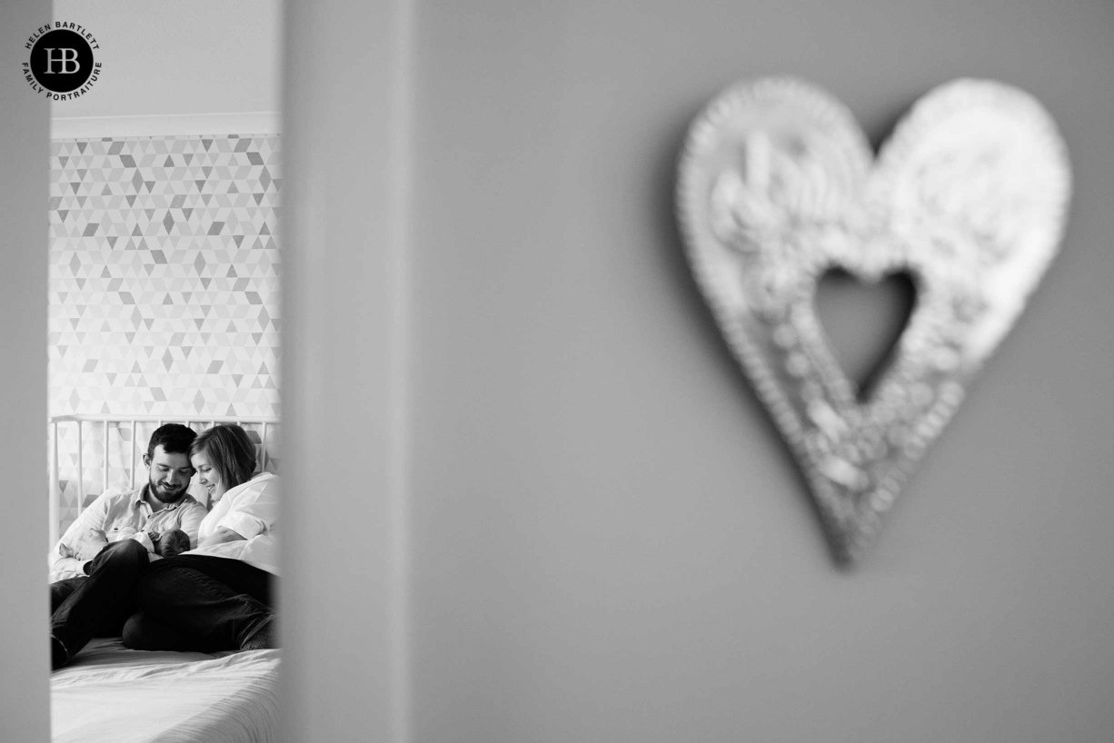 at home newborn pictures are filled with memories, image shows family seen through open bedroom door, heart ornament is on the wall outside room