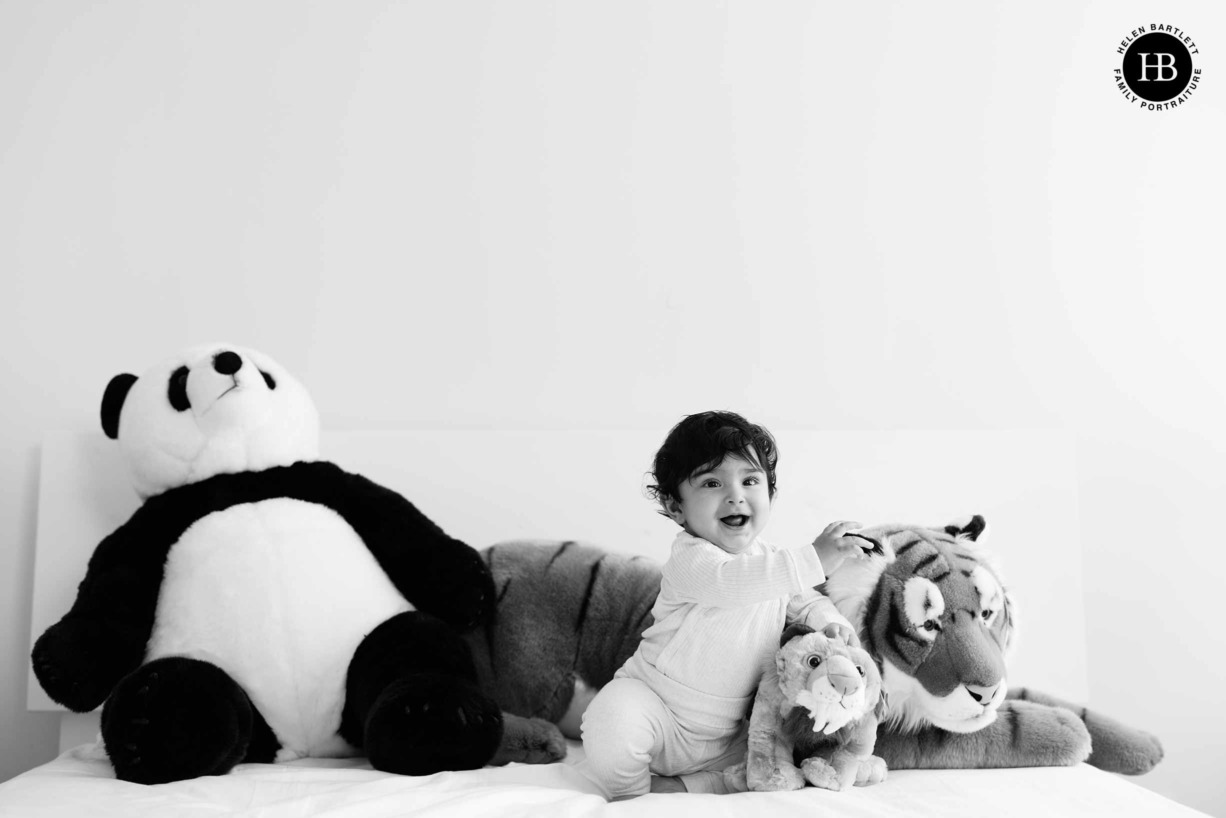 baby plays on parents bed with large stuffed panda, tiger and sober-toothed tiger toys