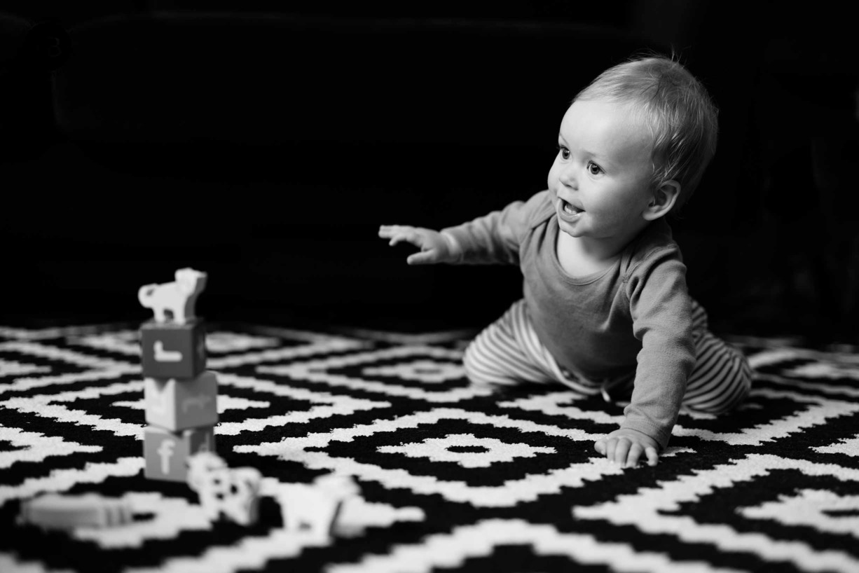 Baby plays with toy building blocks and animals while sitting on black and white patterned rug