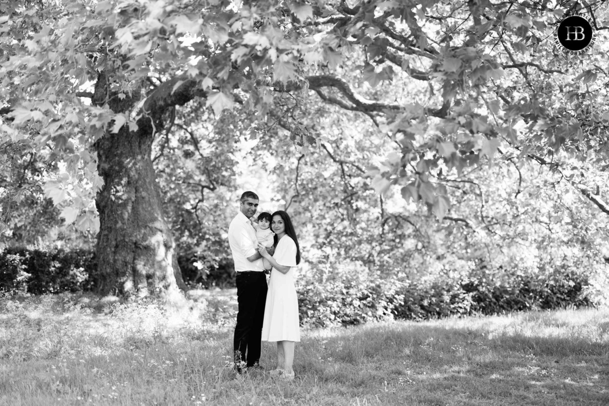 mum dad and baby pose for formal photograph in the trees in London's Hyde Park