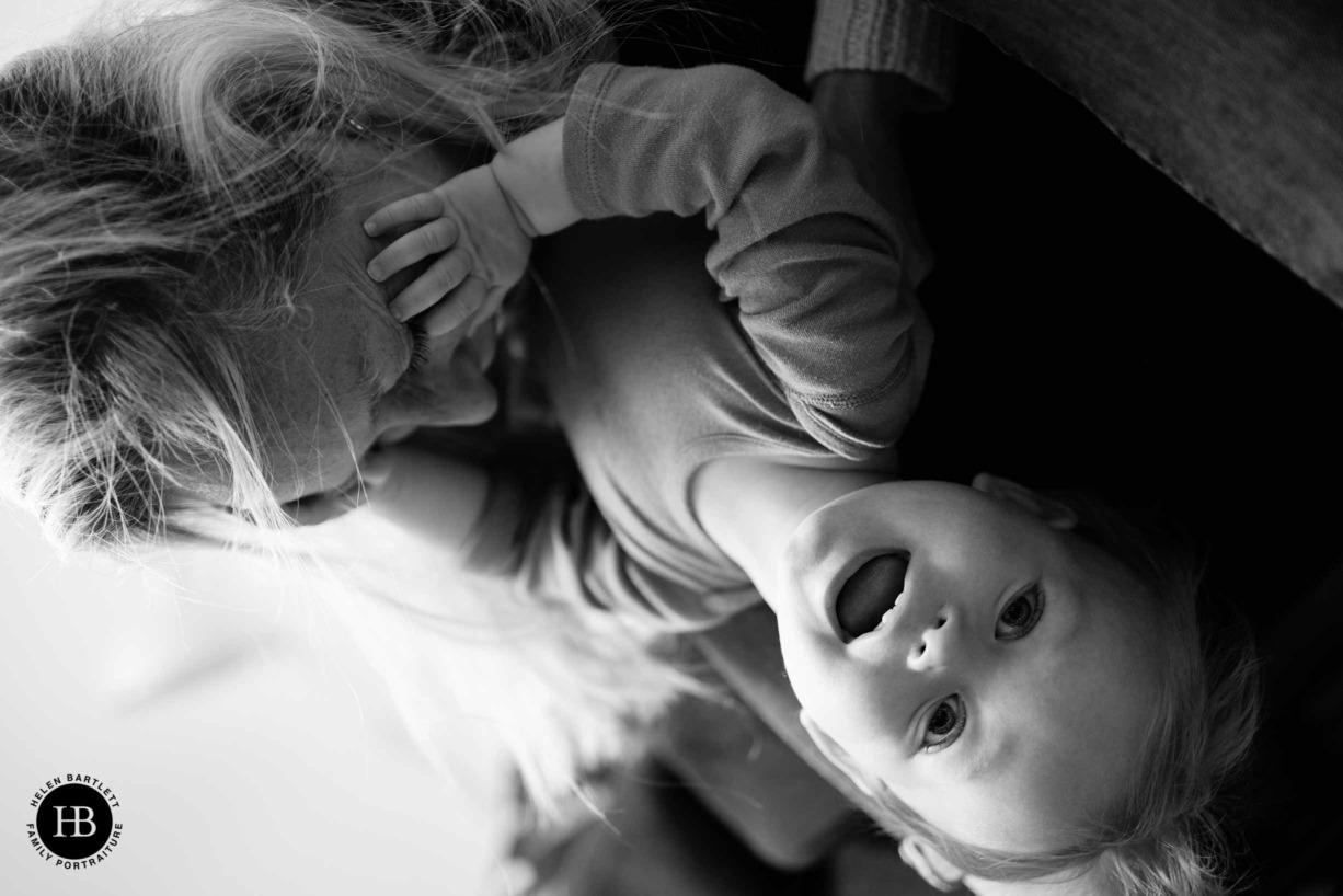 mum and baby play together on family photo shoot. Baby is upside down, mum is kissing his tummy.