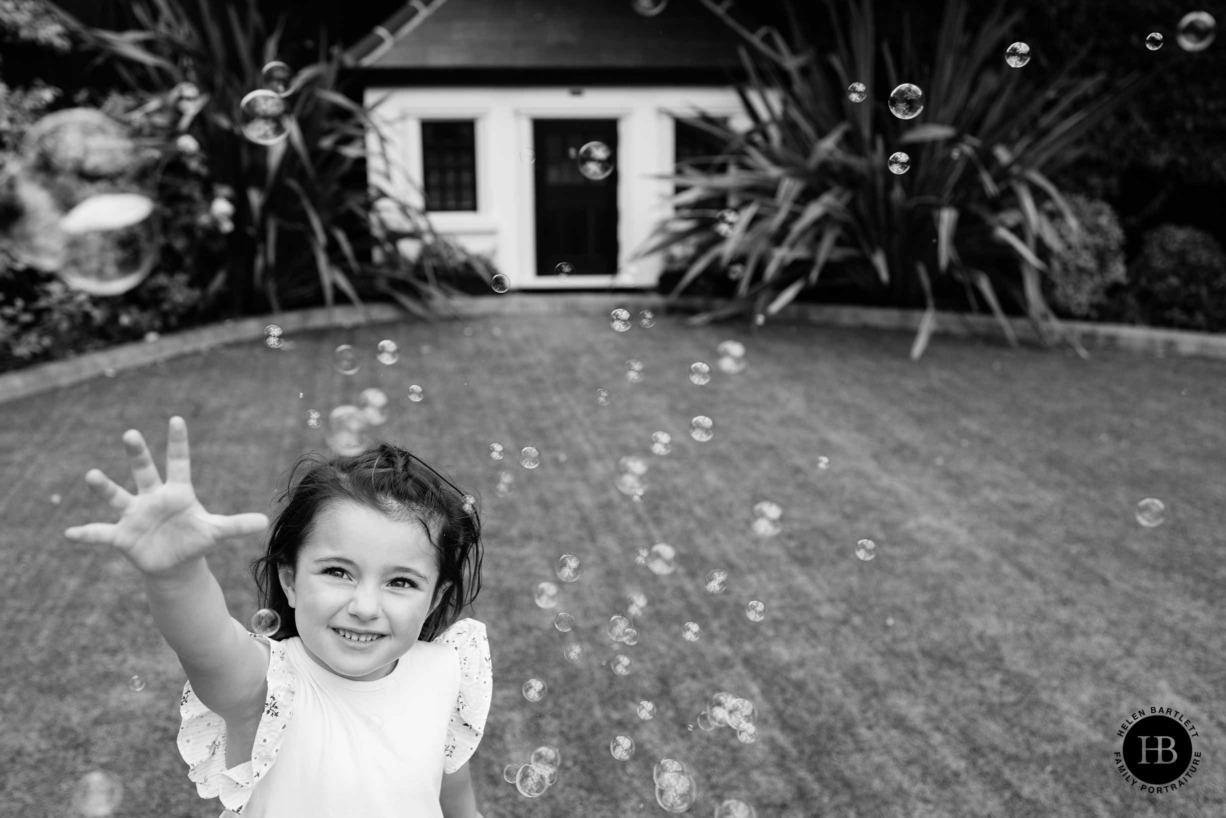 Little girl plays with bubbles in her garden, playhouse visible in the background