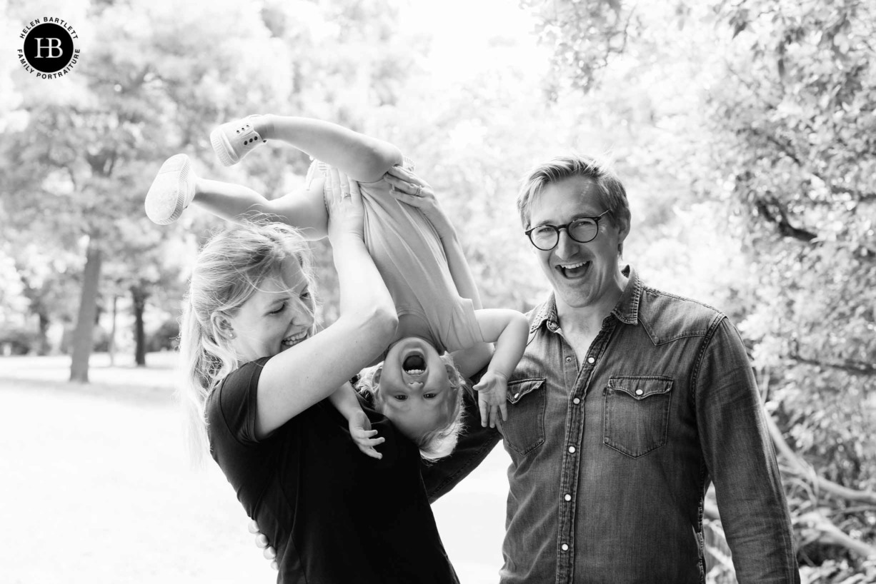 mum holds toddler upside down and dad laughs in joyful family portrait photograph in hackney