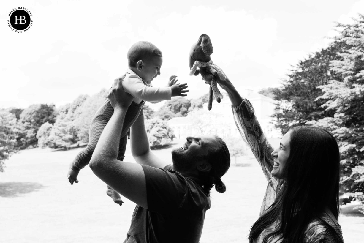 mum and dad play with baby son and a toy elephant on hampstead heath