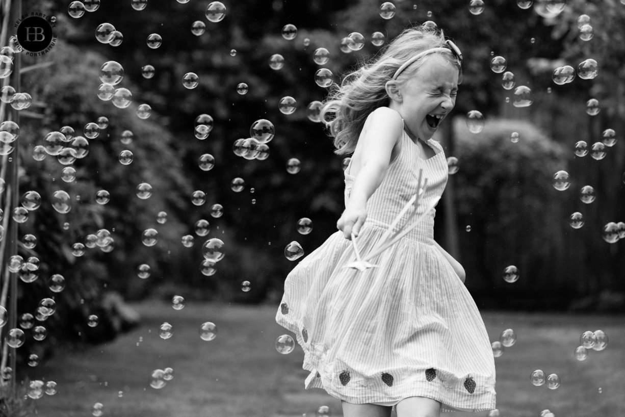 excited-girl-plays-in-bubbles-waving-magic-wand-on-family-photo-shoot