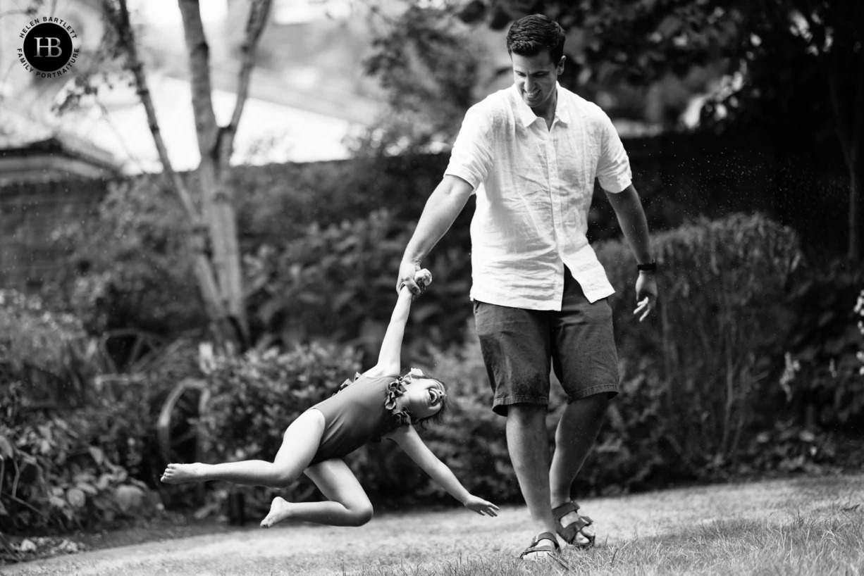 dad-swings-daughter-play-water-spray