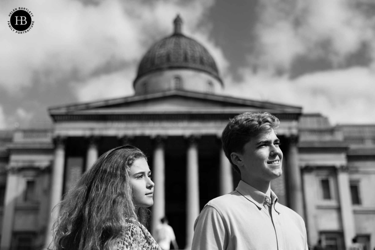 two teenagers stand, faces to the light, in front of the National Gallery in London's Trafalgar square