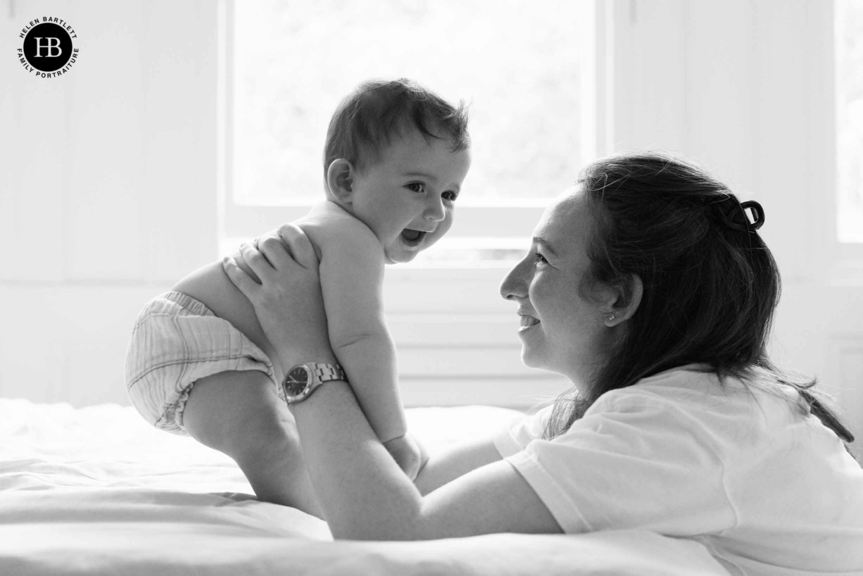 mother-and-baby-laughing-on-bed-window-light